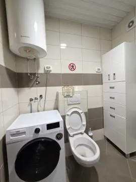 Bathroom equipped with a toilet, washing machine, water heater, and a white cabinet. - image 12