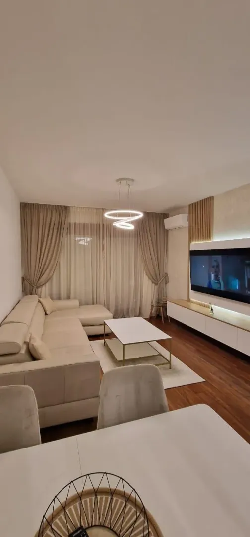Svijetla i moderno namještena dnevna soba sa velikom ugaonom garniturom i televizorom.