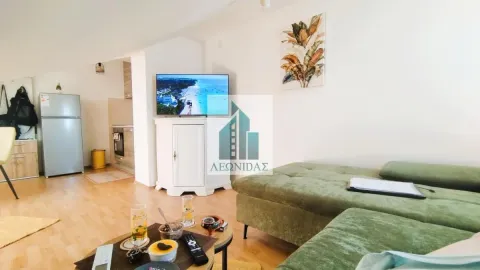 Living room with a sofa, TV, and a view of the kitchen in the background. - image 7