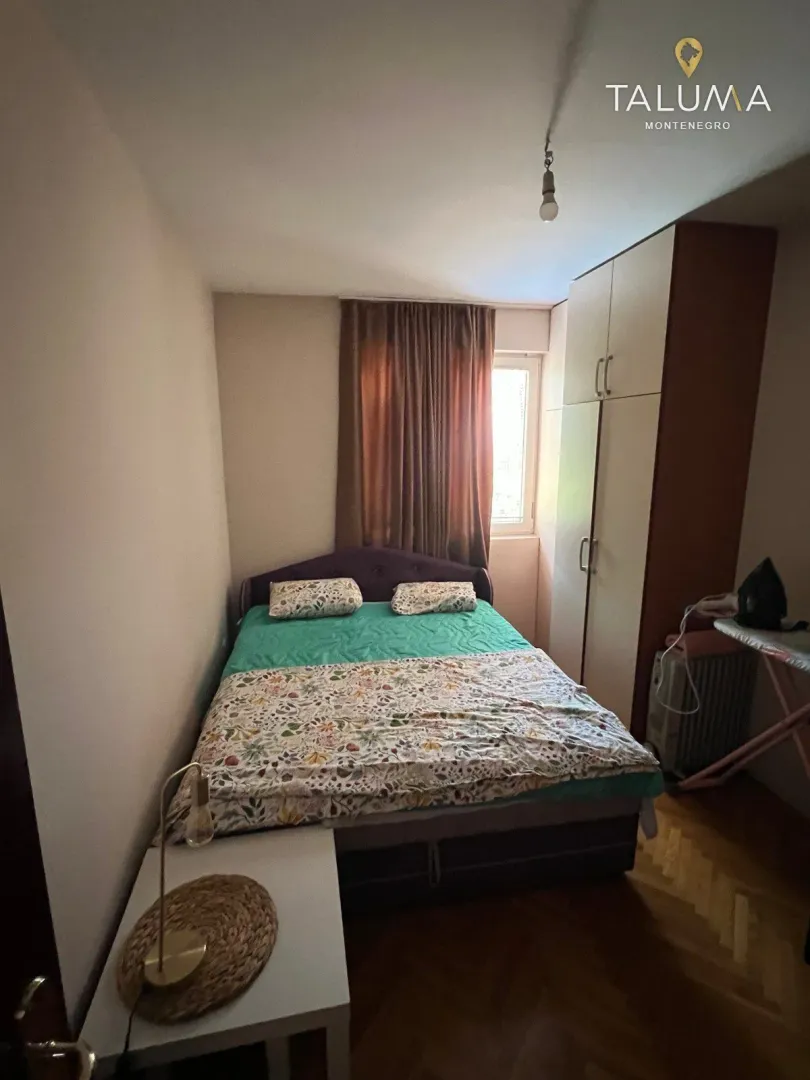 Manja spavaća soba sa bračnim krevetom, ormarom i prozorom.