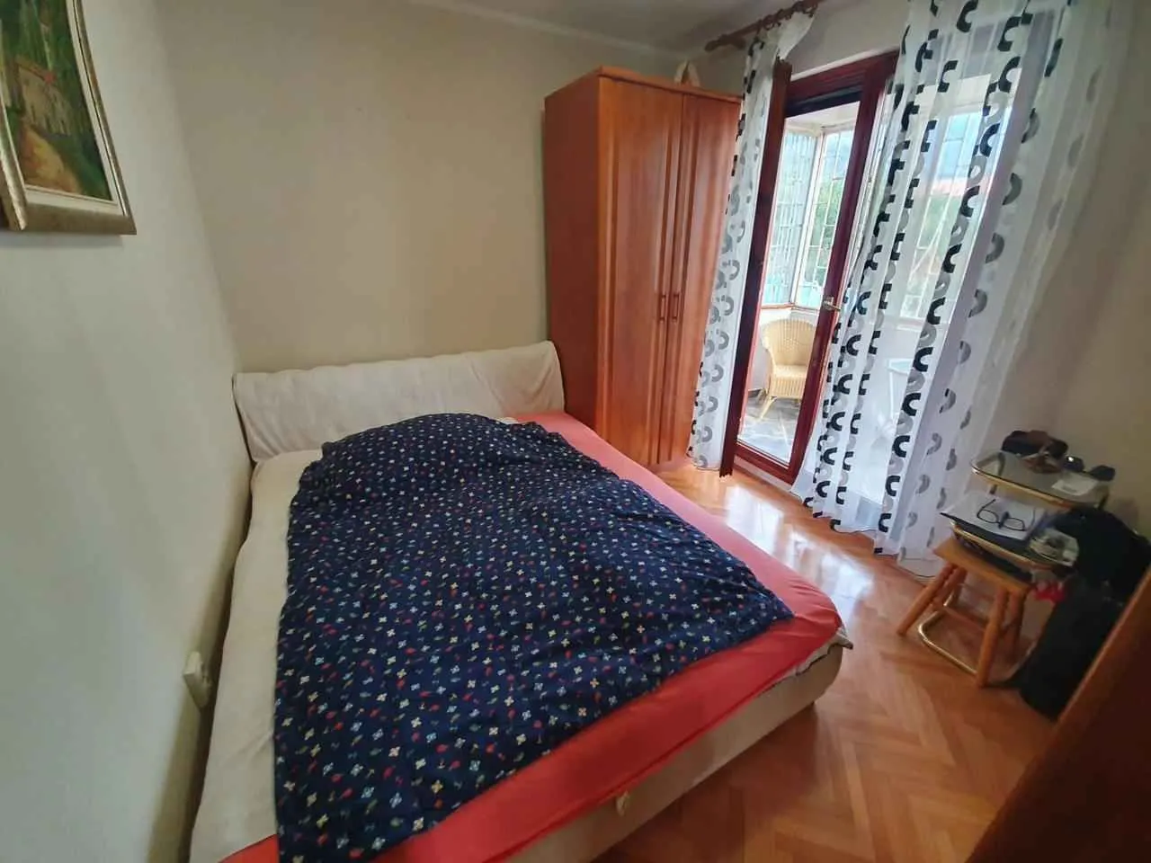 Namještena spavaća soba sa bračnim krevetom, ormarom i izlazom na terasu.