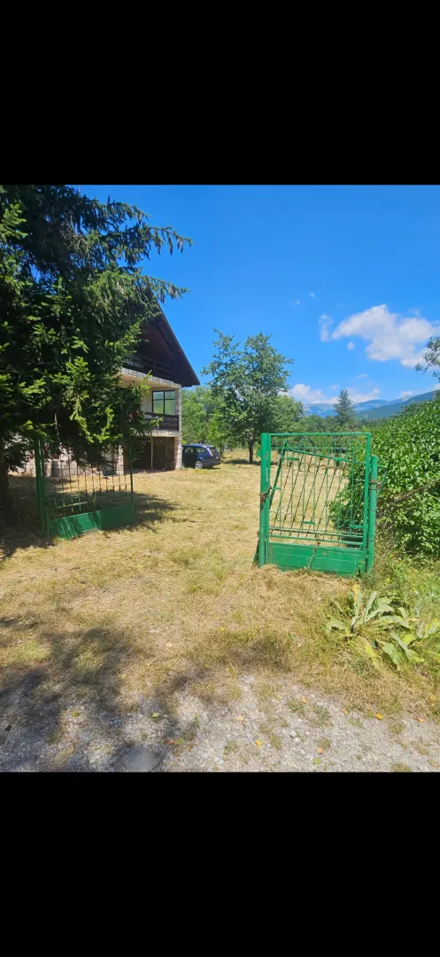 Dvorište sa zelenom ogradom i kućom u pozadini.