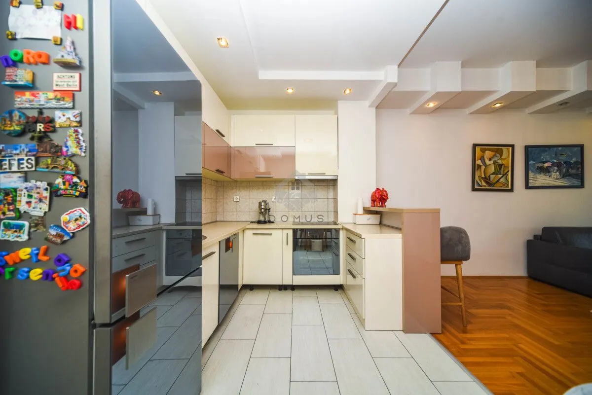 Kitchen equipped with cabinetry and appliances, featuring a breakfast bar separating it from the living room.