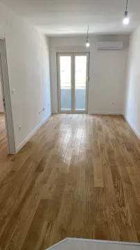 An empty, bright room with wooden flooring and balcony doors. - image 4