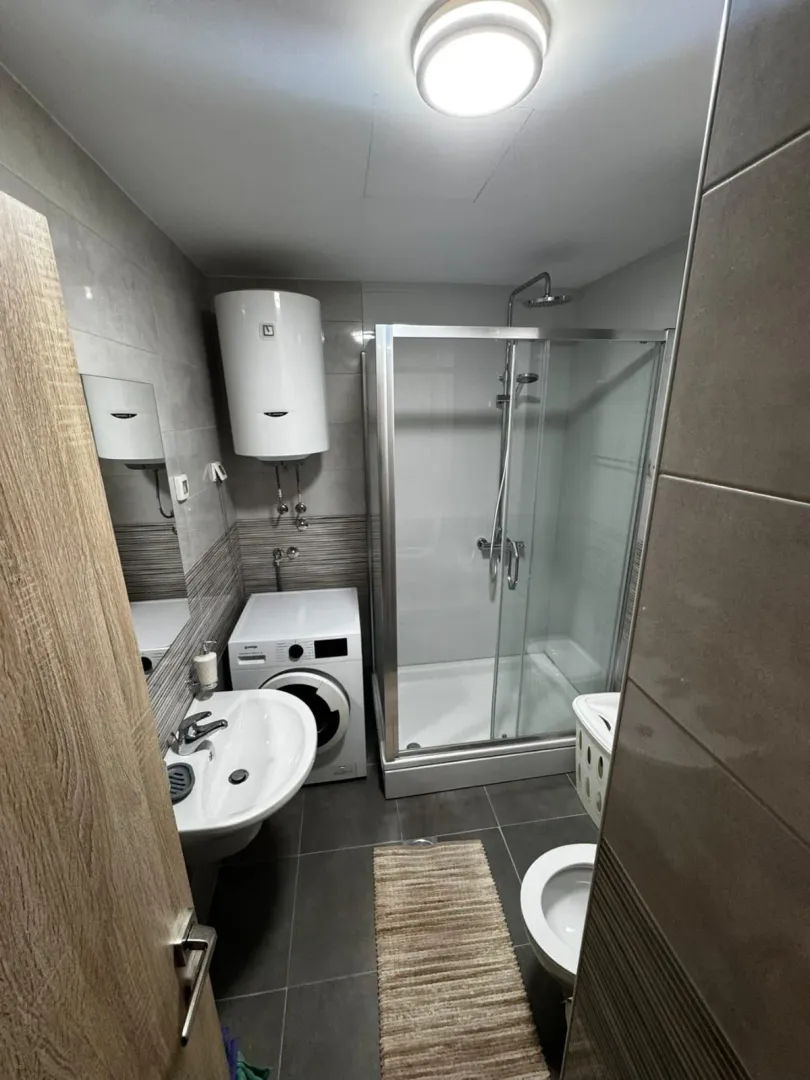 Modern bathroom with a shower cabin, sink, washing machine, and toilet.