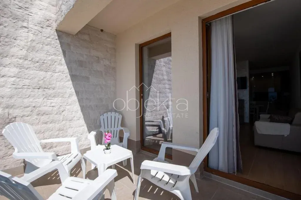 Small covered terrace with white plastic furniture and a view of the apartment interior.