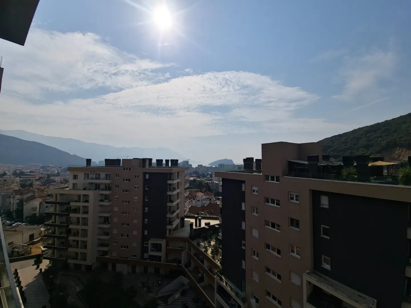 Pogled sa terase na okolne stambene zgrade i brda u pozadini.