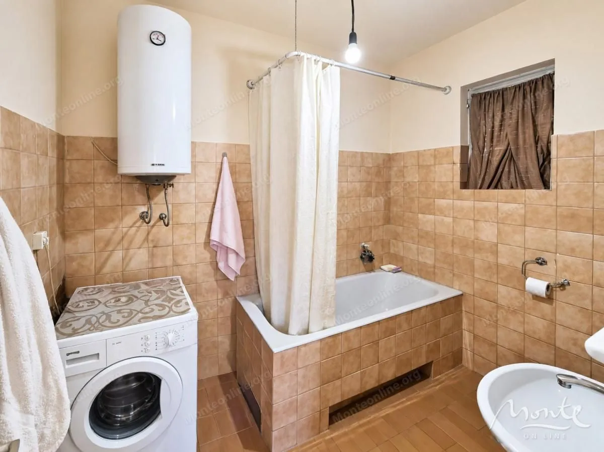 Kupatilo obloženo keramičkim pločicama sa kadom, veš mašinom i bojlerom.
