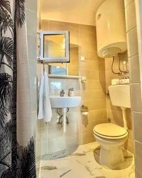 Small bathroom tiled with ceramic tiles featuring a sink and a toilet. - image 9