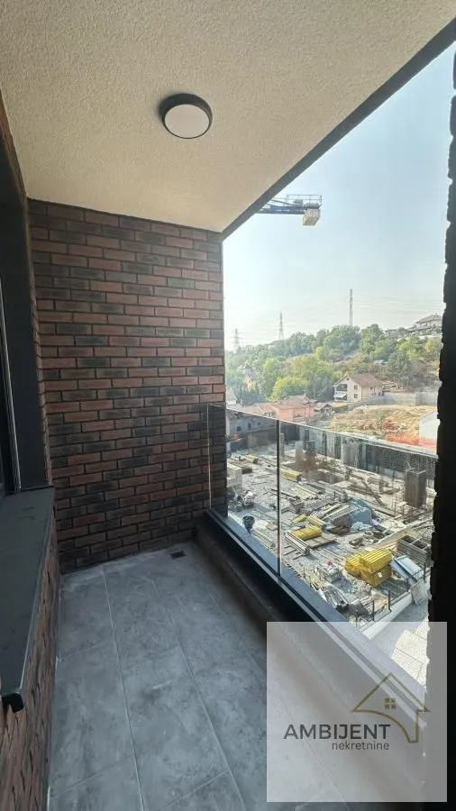 Natkriveni balkon sa staklenom ogradom i pogledom na okolinu.