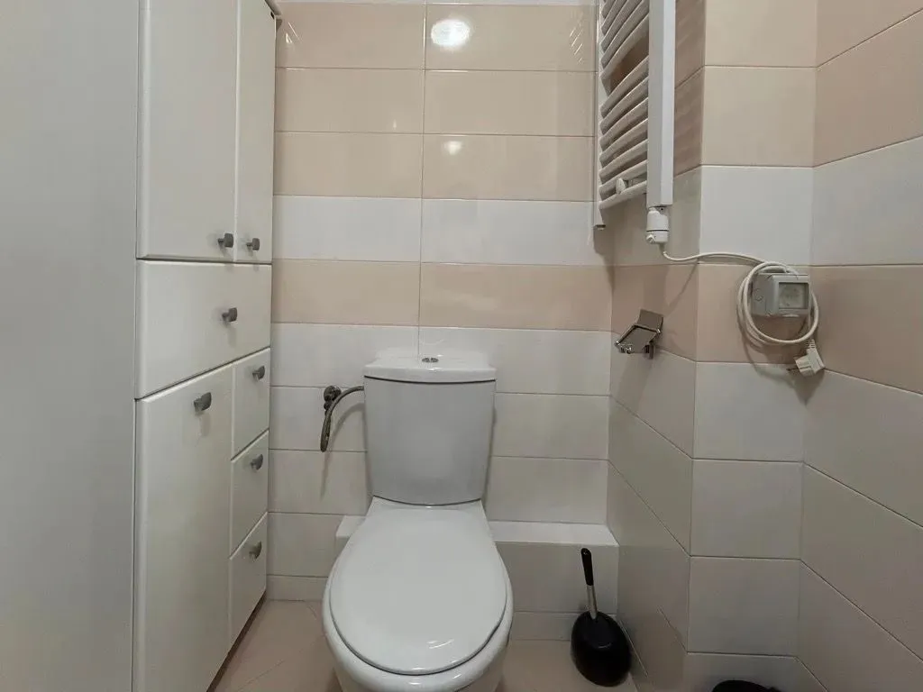 Compact bathroom with a toilet, built-in cabinet, and towel warmer.