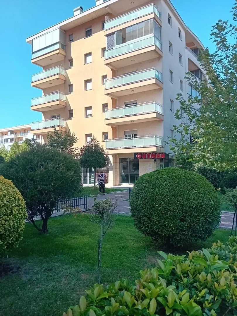 Vanjski izgled višespratne stambene zgrade sa uređenim dvorištem.