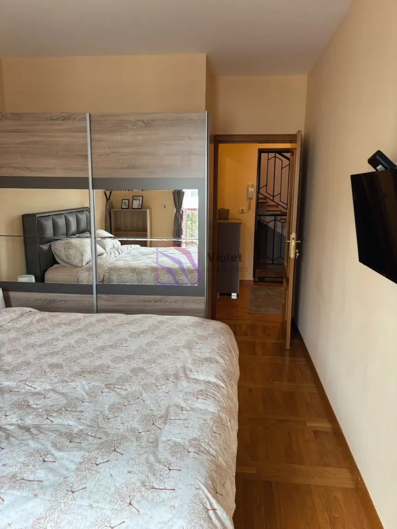 Spavaća soba sa velikim bračnim krevetom, plakarom sa ogledalom i TV-om na zidu.