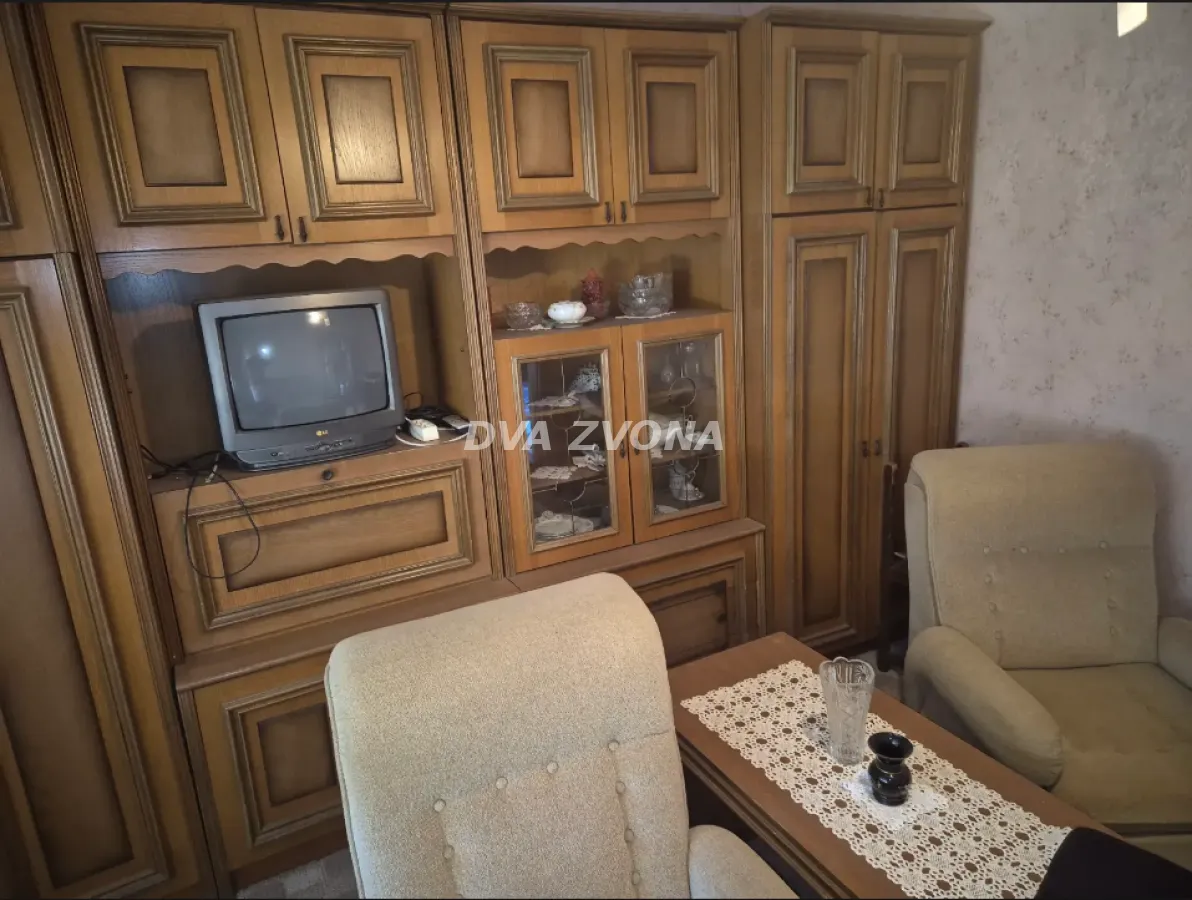 Dnevna soba sa drvenim nameštajem, foteljama i starim televizorom.