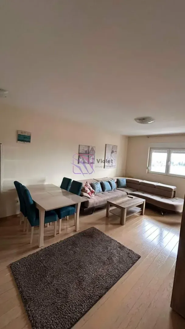 Dnevna soba sa garniturom, trpezarijskim stolom i prozorom.