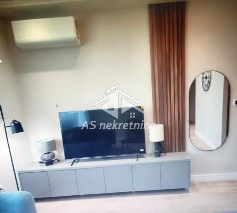 Dnevna soba sa TV komodom, televizorom i klima uređajem na zidu.