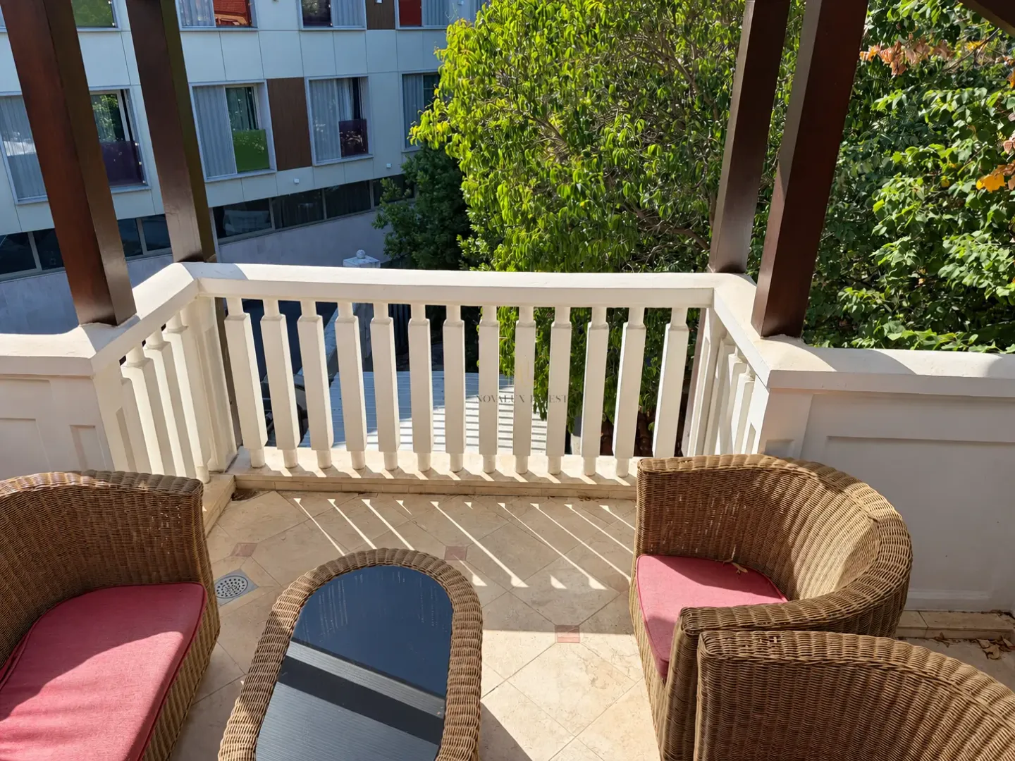 Covered terrace furnished with rattan seating and a view of greenery.