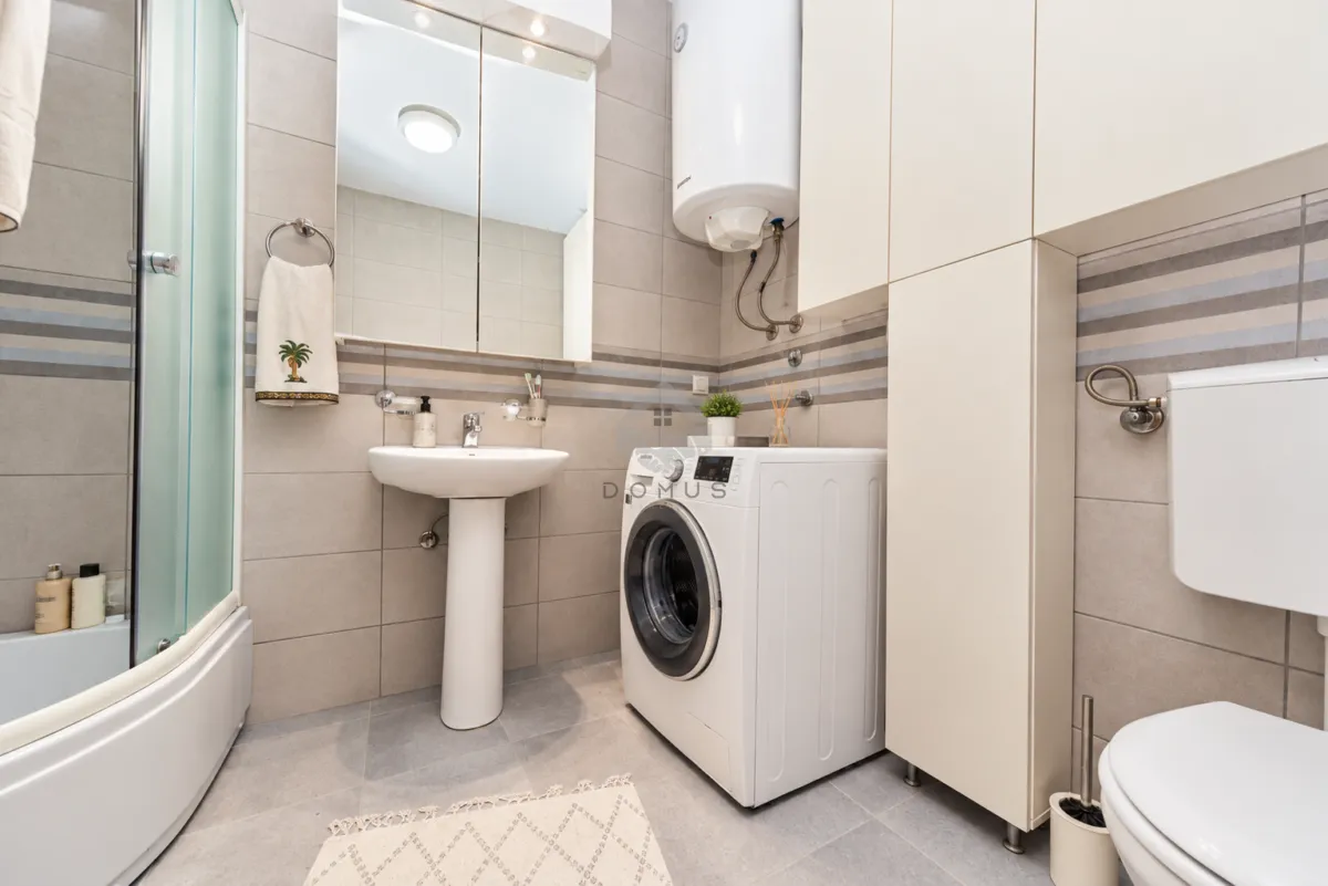 Bathroom equipped with a shower cabin, washbasin, washing machine, and toilet.