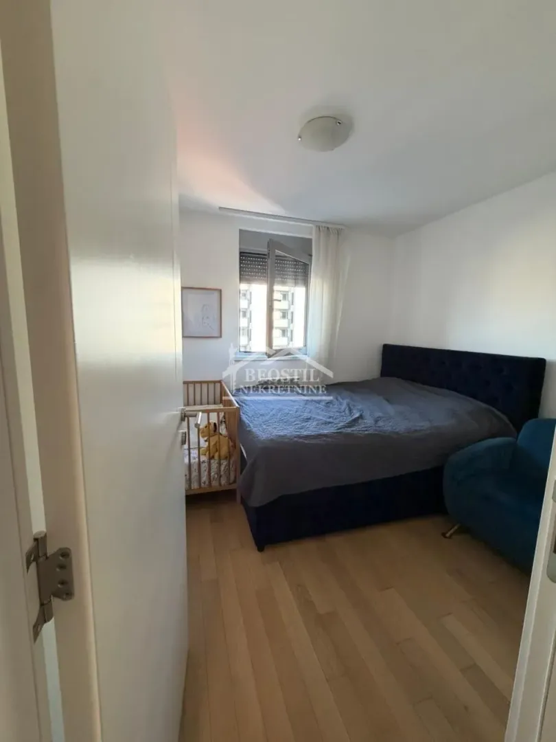 Pogled na spavaću sobu sa bračnim krevetom, krevetcem i prozorom.