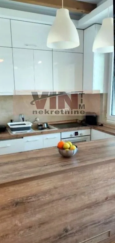 Moderna kuhinja sa belim elementima i šankom od drveta.