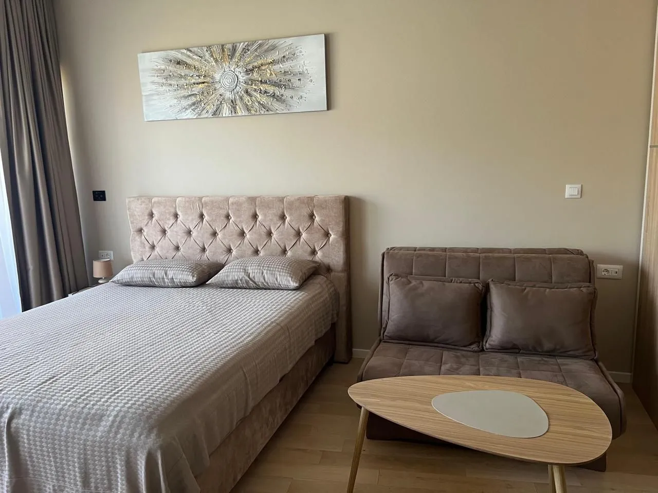 Furnished bedroom with a double bed, fold-out armchair, and a decorative painting on the wall.