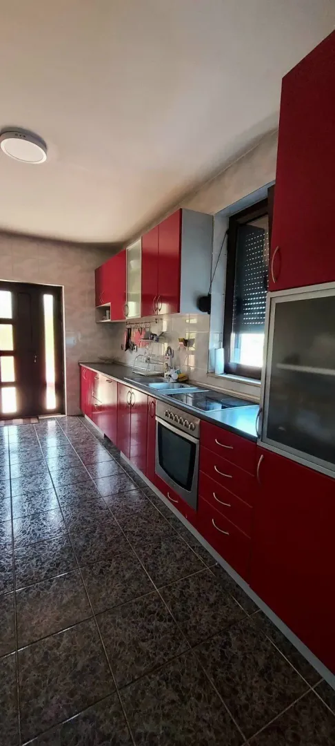 A long kitchen with red cabinets and tiled flooring.