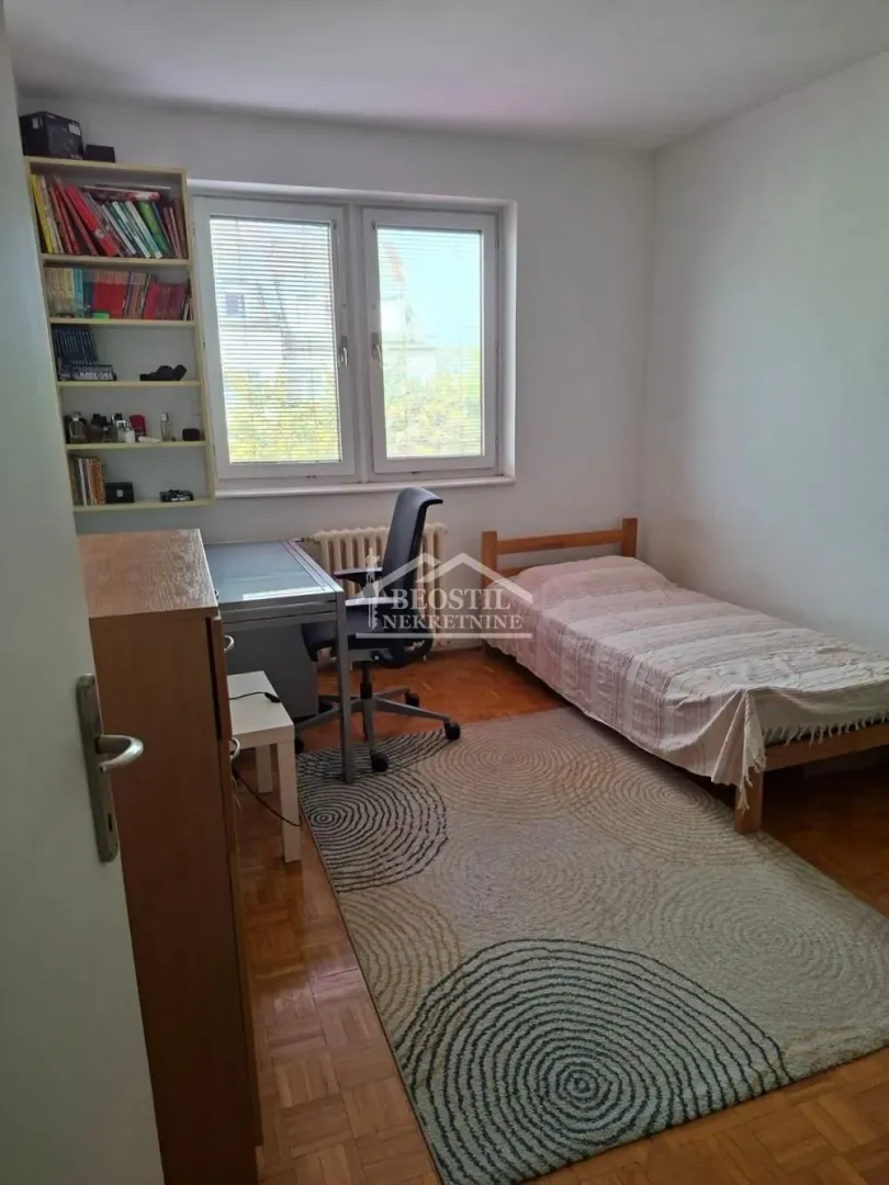 Nameštena spavaća soba sa krevetom, radnim stolom i policom za knjige.