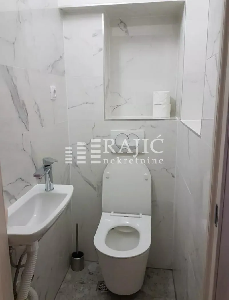 Small bathroom with toilet and washbasin tiled in marble-patterned tiles.