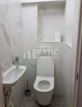 Small bathroom with toilet and washbasin tiled in marble-patterned tiles. - image 7