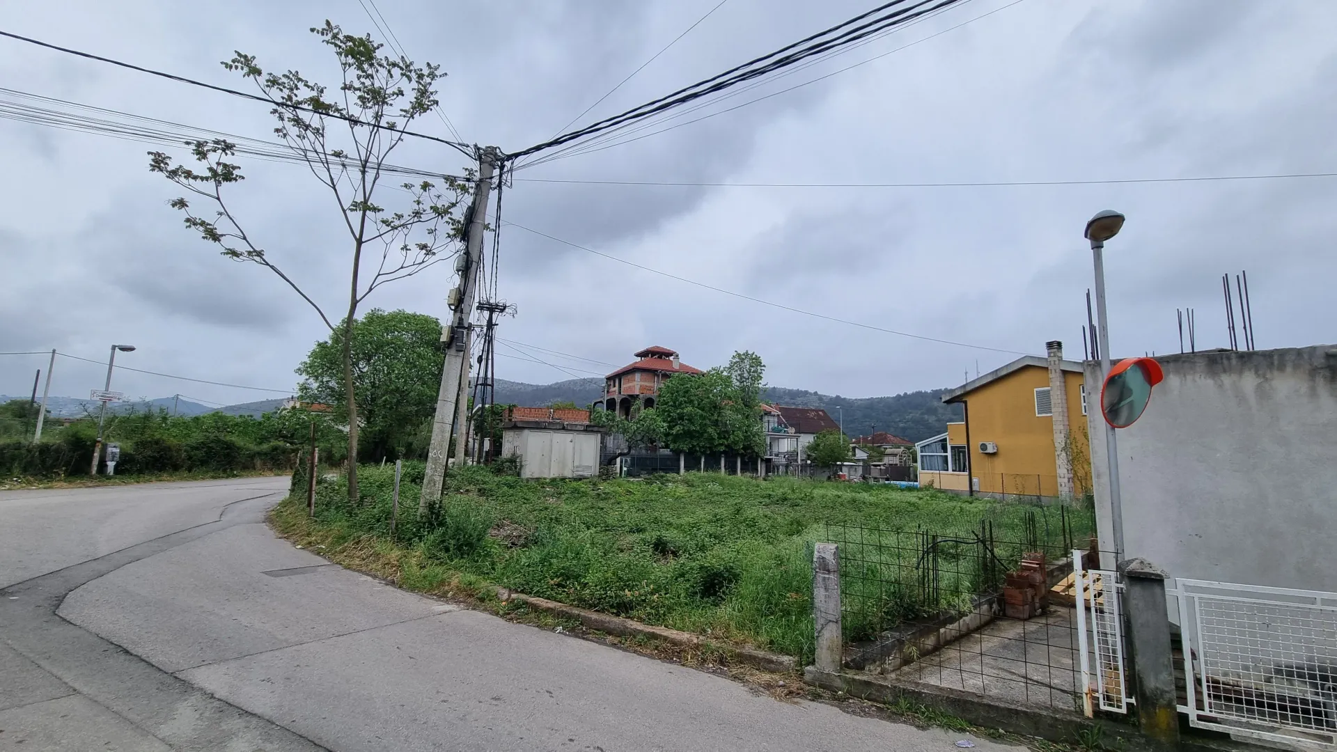 Pogled na plac i okolne kuće pored asfaltnog puta.