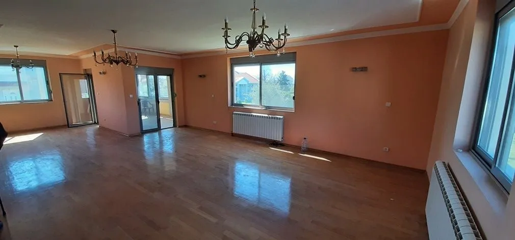 Spacious empty living room with parquet flooring and chandeliers on the ceiling.