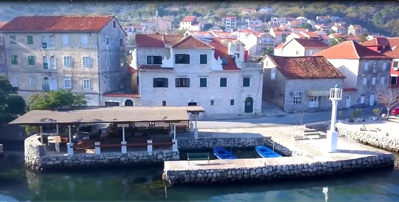 Pogled iz vazduha na kamene kuće pored obale i mol sa čamcima.