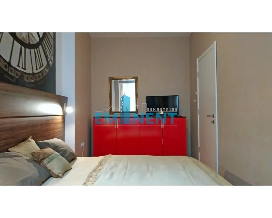 Furnished bedroom with a double bed, a red chest of drawers and a TV.