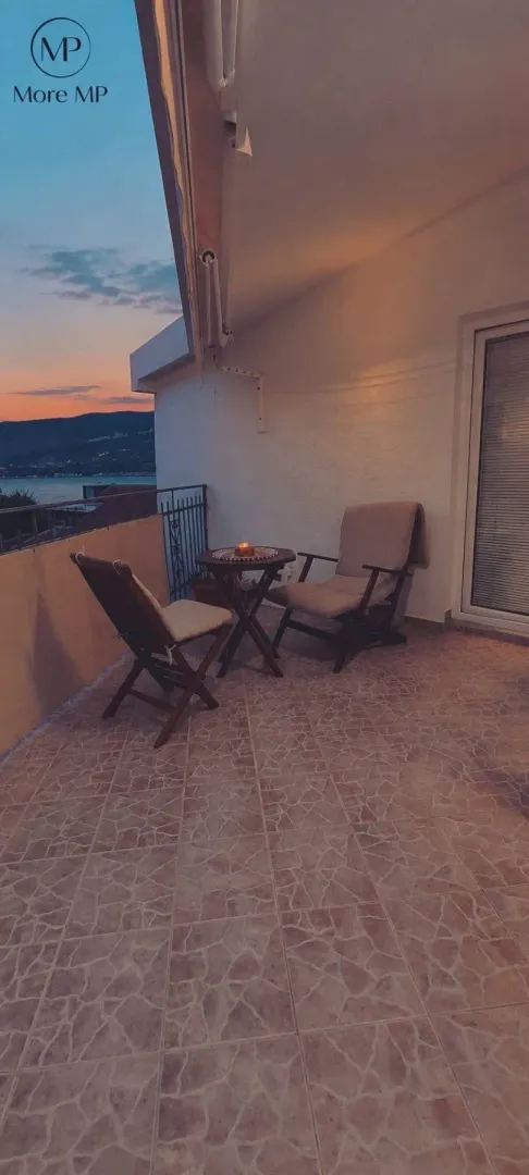 Namještena terasa sa stolom i stolicama i pogledom na more u sumrak.
