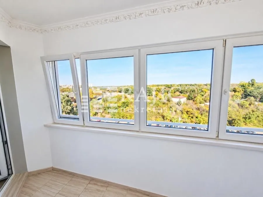Enclosed balcony with a view of greenery and the city.