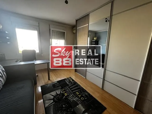 Spavaća soba sa krevetom, radnim stolom i velikim ugradnim plakarom.