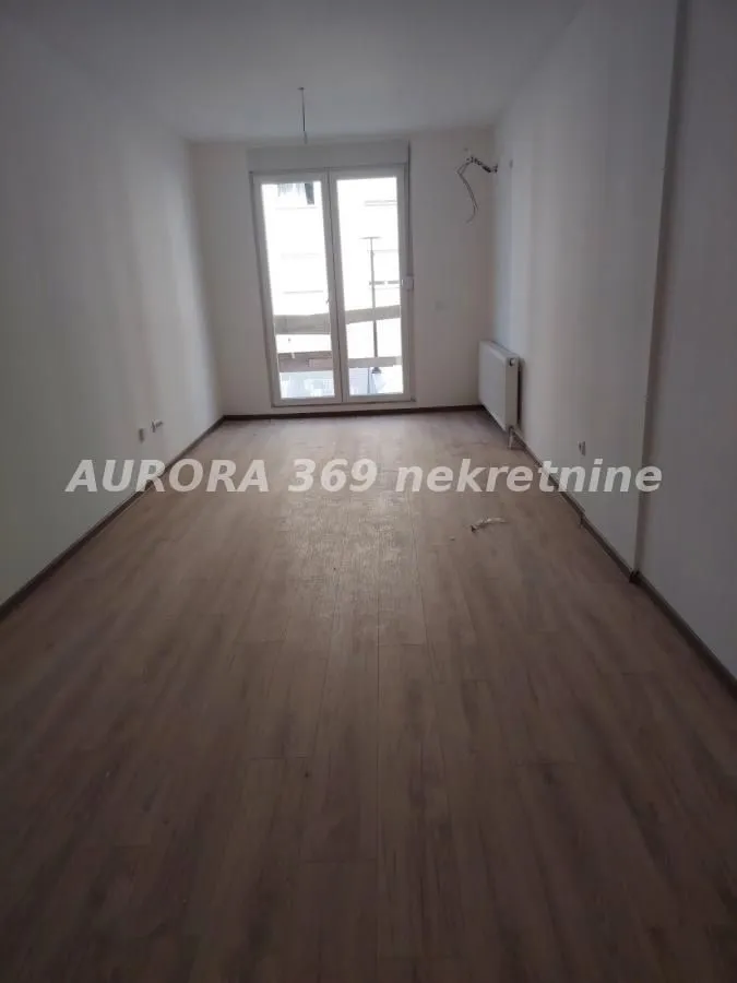 Prazna neopremljena prostorija sa laminatom na podu i izlazom na terasu.