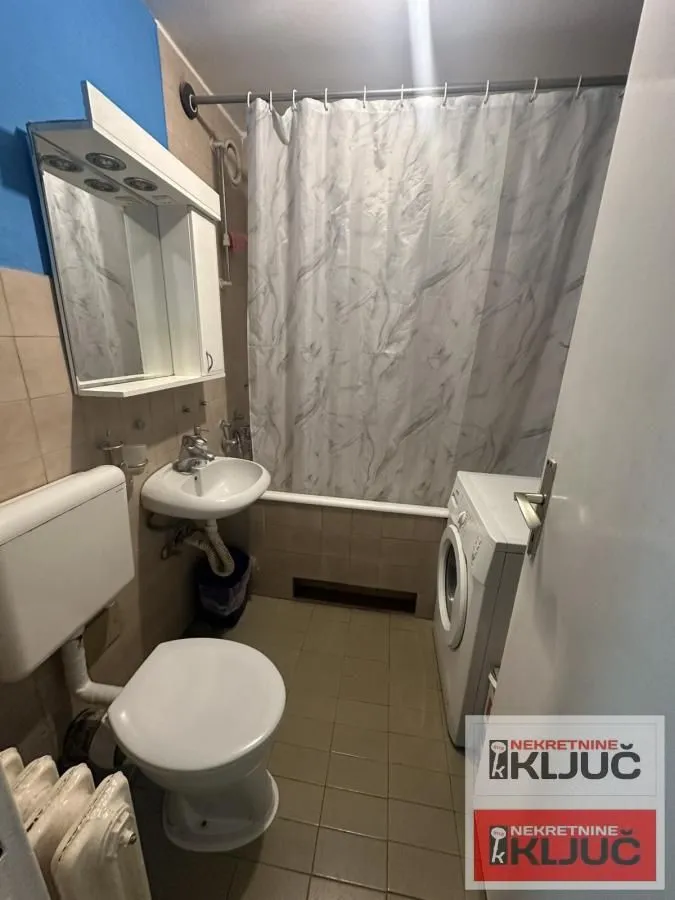 Manje kupatilo sa kadom, umivaonikom, WC šoljom i veš mašinom.
