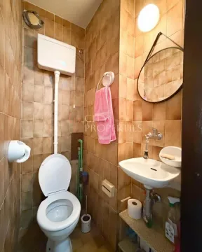 Manje kupatilo obloženo braon pločicama sa wc šoljom, umivaonikom i ogledalom. - image 8