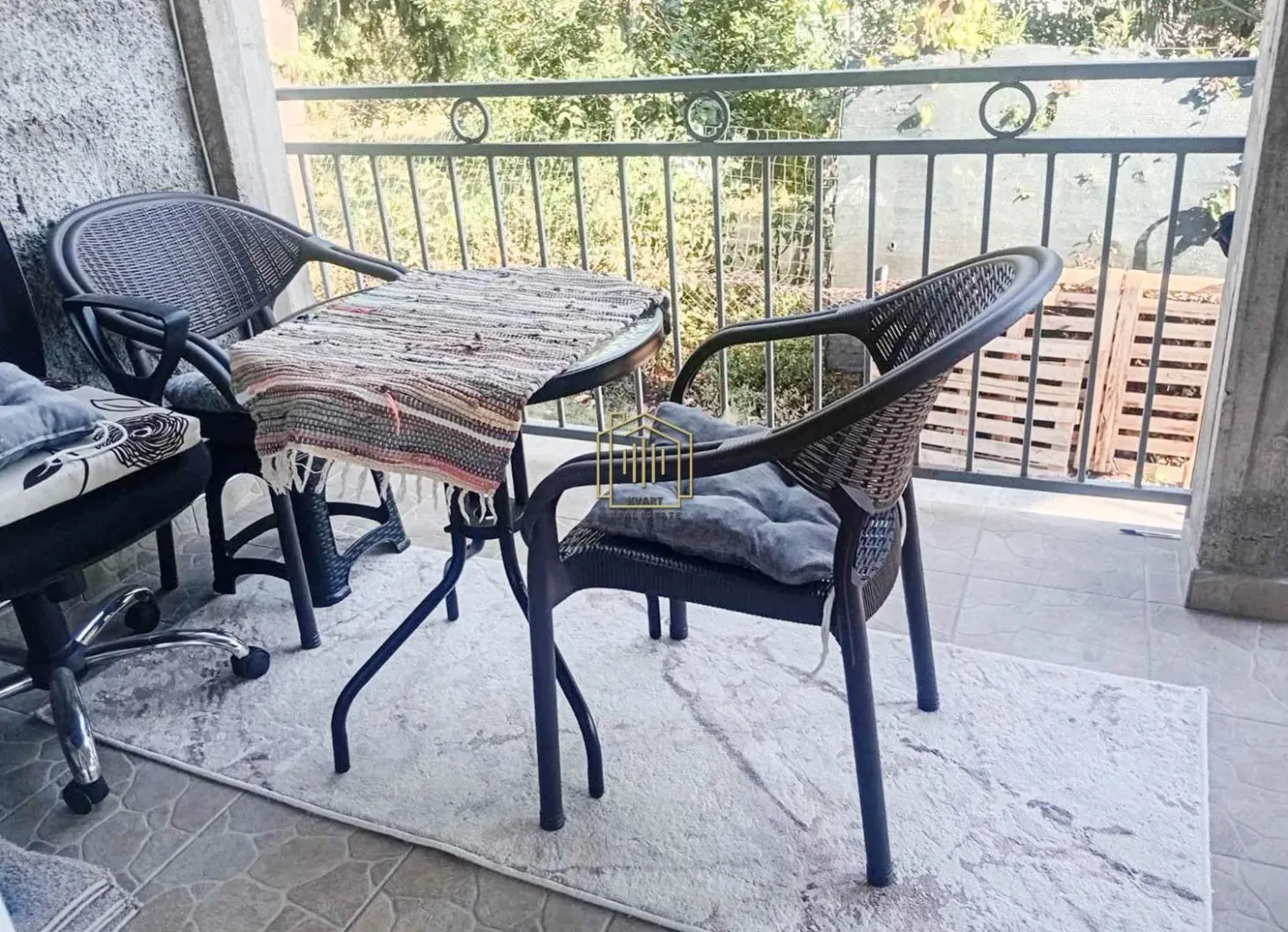 Small table and two chairs on a covered balcony with a metal railing.
