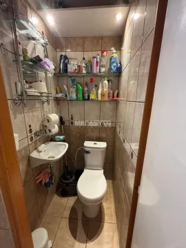 Small bathroom with a toilet, washbasin, and wall shelves with hygiene products. - image 4