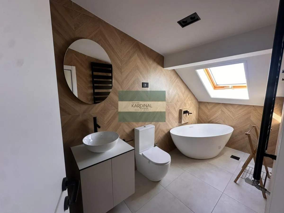 Moderno opremljeno kupatilo sa kadom, umivaonikom i wc šoljom pod kosinom krova.