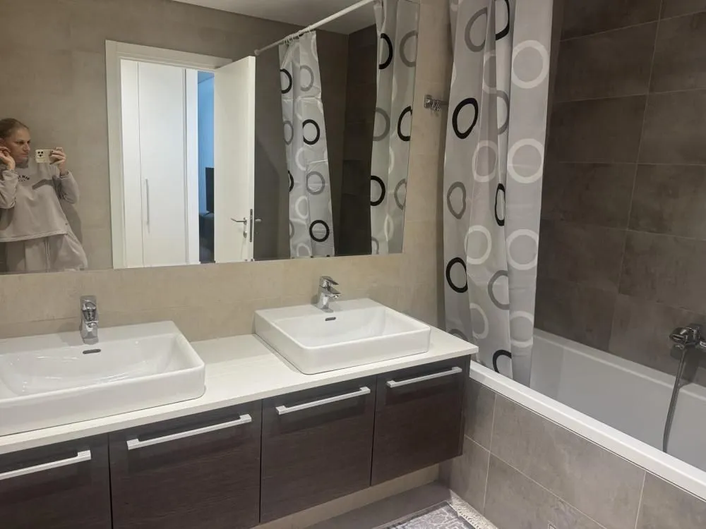 Bathroom with two washbasins, mirror, and bathtub with a curtain.