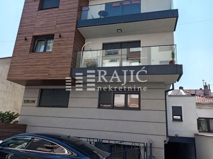 Exterior view of a modern residential building with a balcony and a parked car in front.