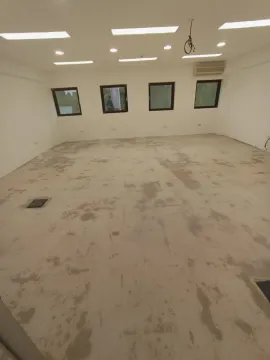 A spacious empty room under construction with windows and ceiling lights. - image 3