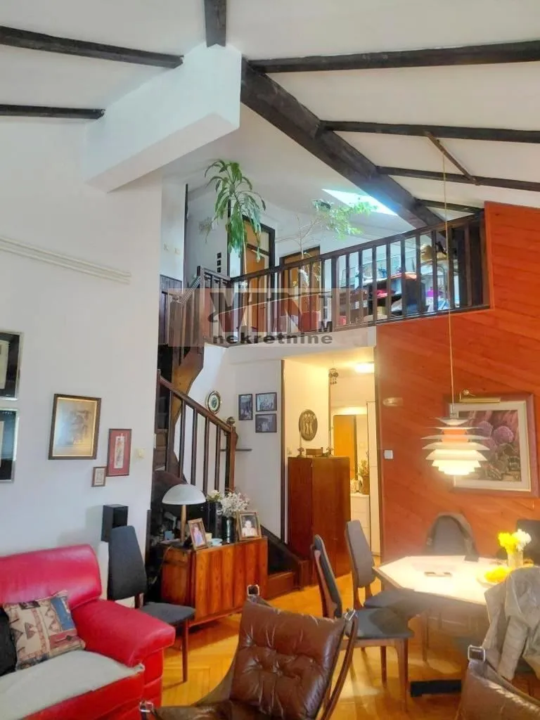 Living room with a dining area, wooden staircase, and an upper-floor gallery.