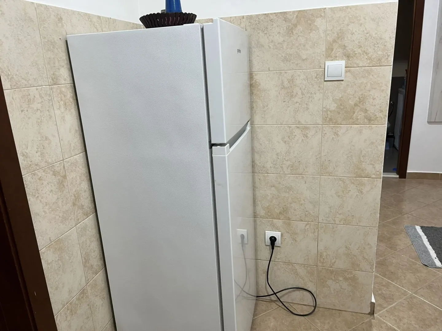 A refrigerator in the corner of a tiled room.