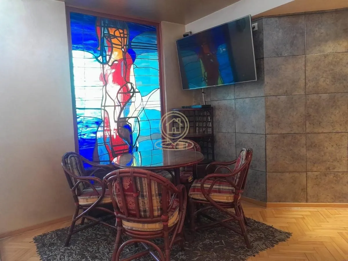 Living room with a dining table, a large stained glass window and a wall-mounted TV.