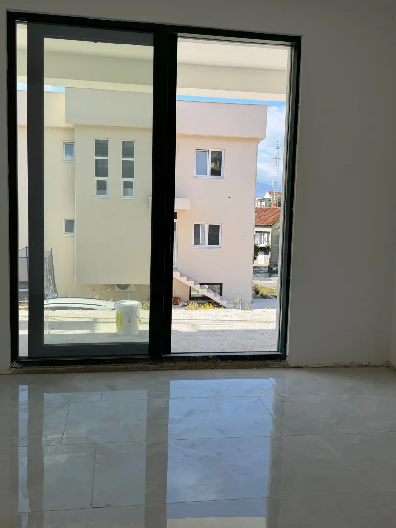 View through a large balcony door towards the exterior space and neighboring houses.
