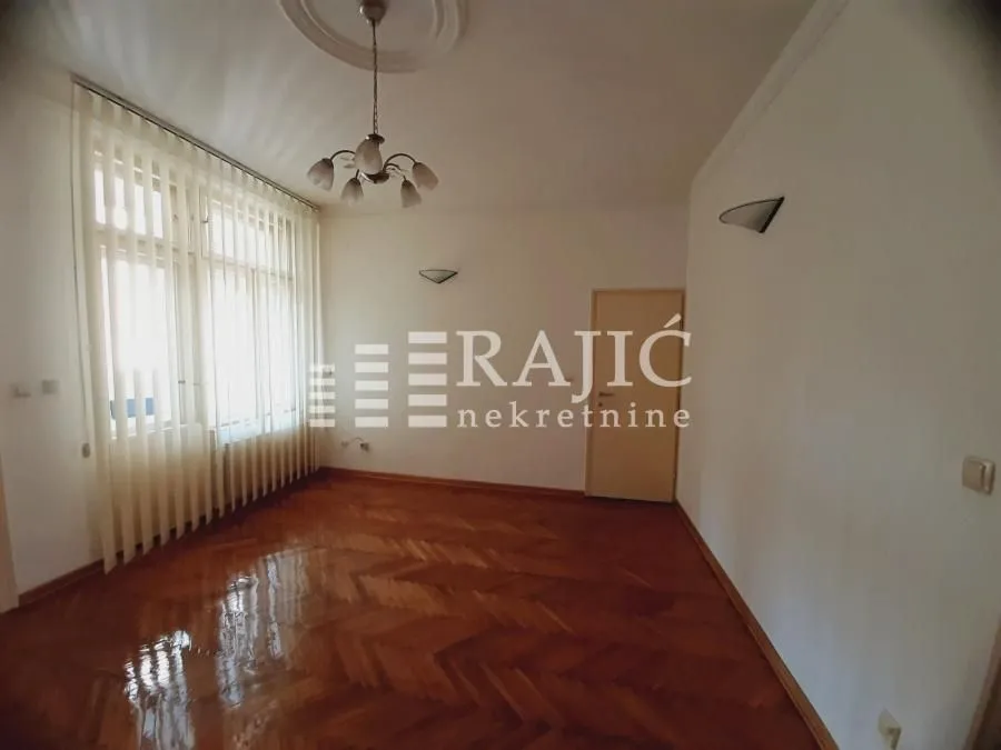Empty room with parquet flooring and a large window.
